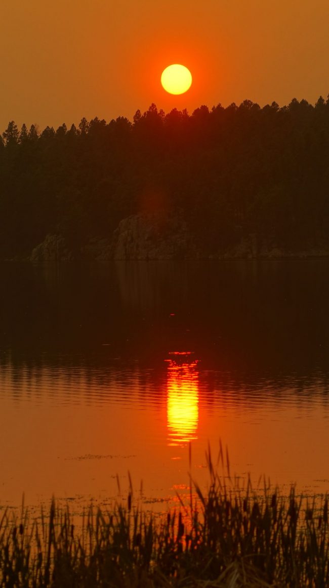 Orange wildfire sunset in the sky, and also reflected in a lake.