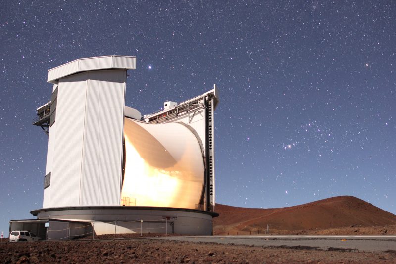 Large telescope with hills and starry sky behind it.