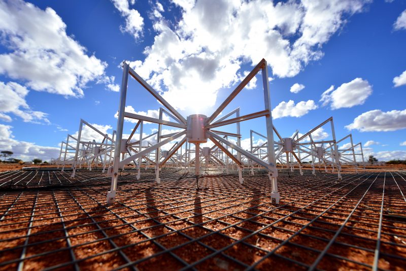 Spider-like standing structures in field with blue sky and puffy clouds overhead.