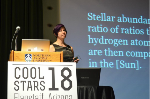 Woman standing in front of projector screen with large sign in front of her.