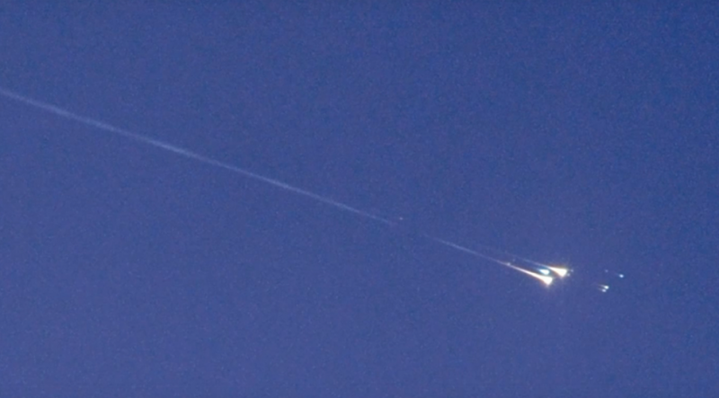 A fiery meteor flashing across a daylight sky with parts seeming to explode off.