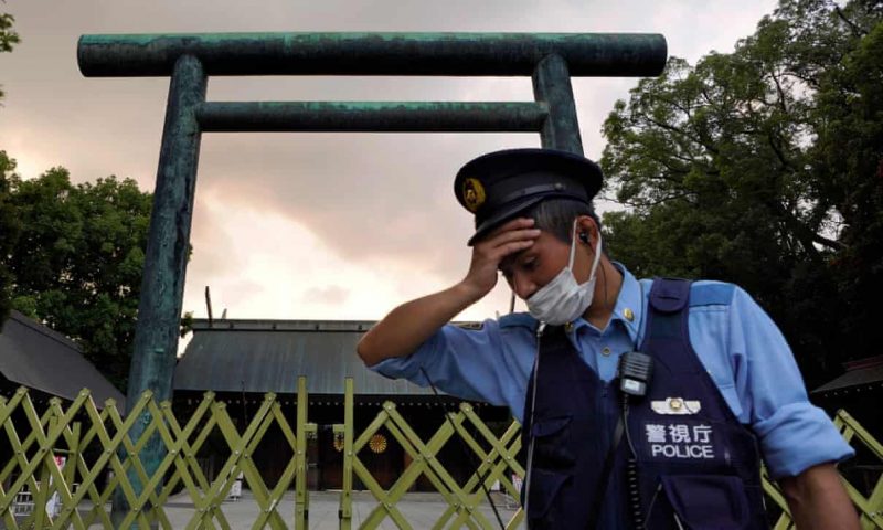 A man in police cap and vest, with tall Japanese structure in background.