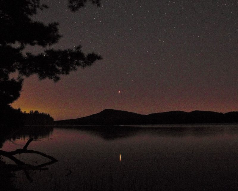 A ridgeline in the background, a lake in the foreground, and red Mars reflecting in the lake.