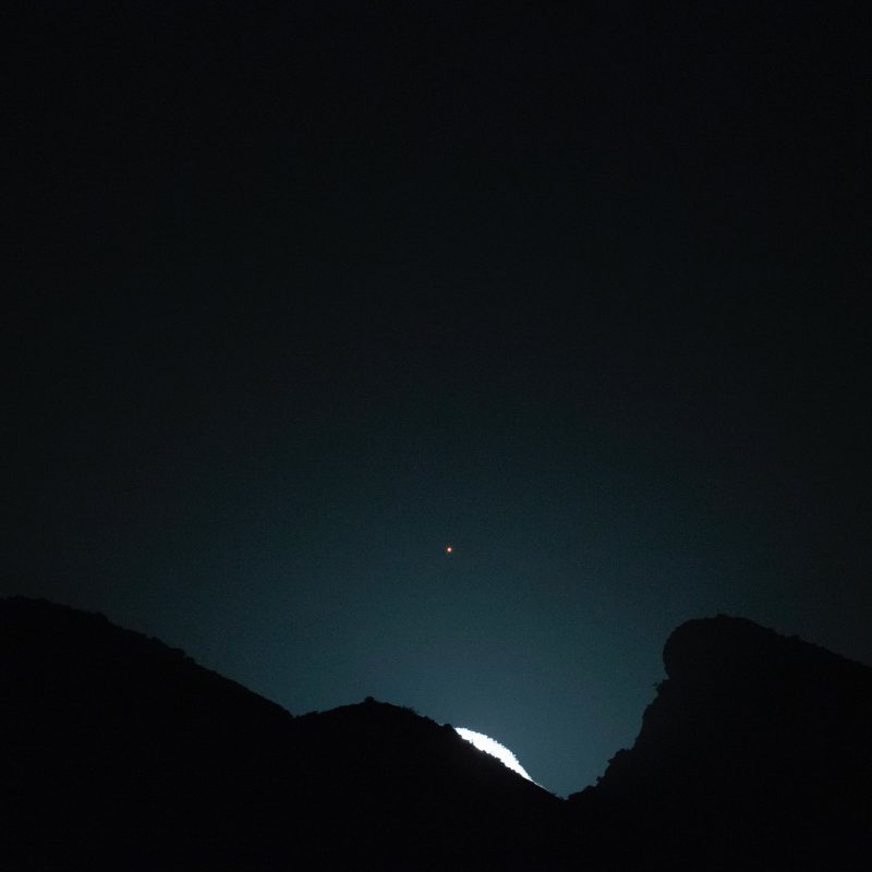 The edge of the bright moon appearing above a ridgeline, with reddish dot of Mars above.