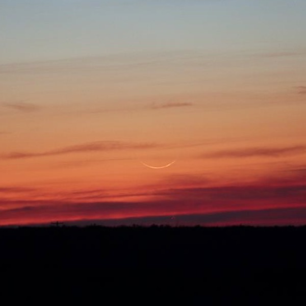 A barely visible crescent moon set against bright twilight.