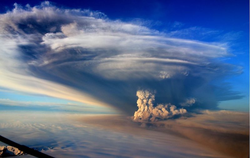 Huge billowing mushroom cloud, many miles in extent, flattening out at the top, against blue sky.