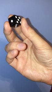 A hand holding a standard die with white dots on black.