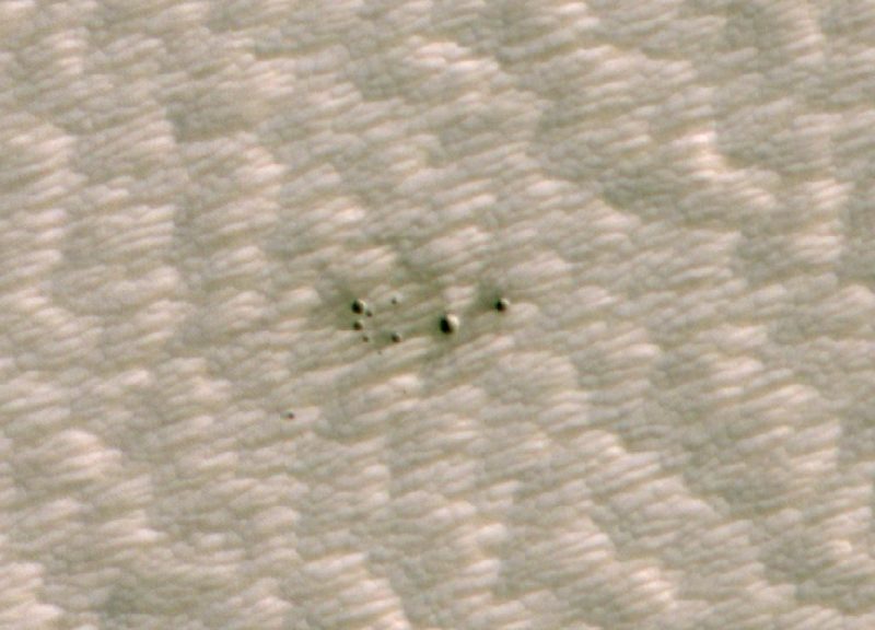 A cluster of small meteor craters on terrain with linear features.