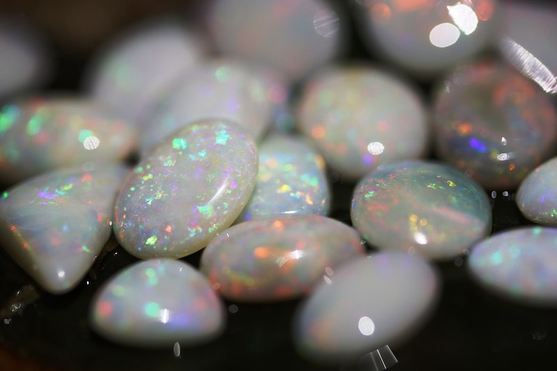October birthstone: Several polished oval opals, primarily white with iridescent blue, green, yellow and red specks.