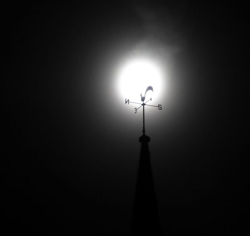 Harvest Moon behind a weather vane with four arms and a flat metal rooster on top.