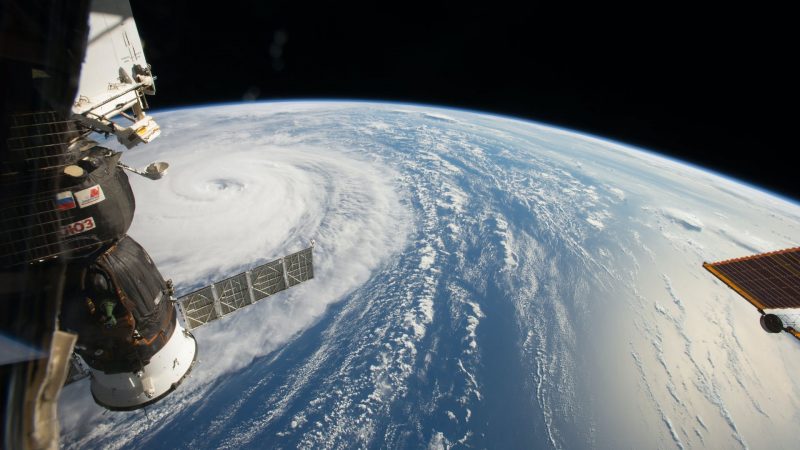 Earth's vast oceans are covered in a swirl of clouds, with components of the ISS visible from the side.