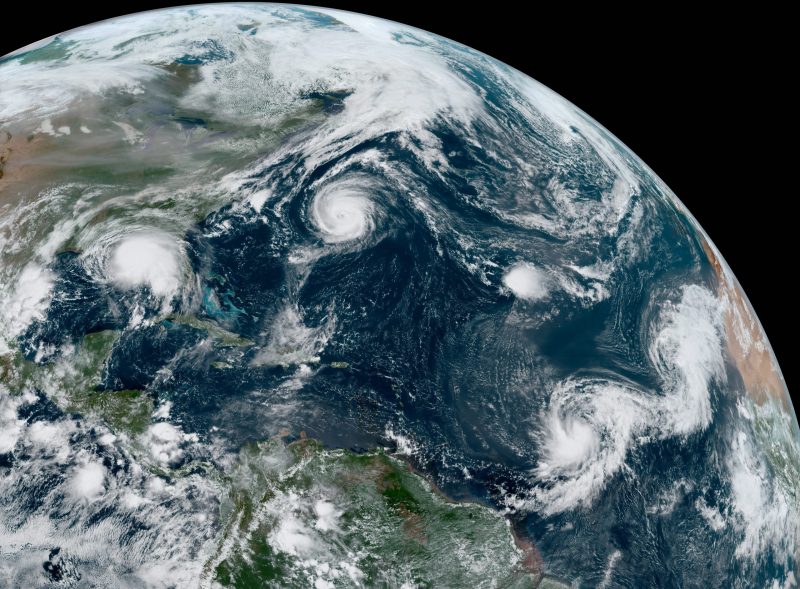 Vista satélite do Oceano Atlântico mostrando 5 tempestades tropicais circulares brancas.
