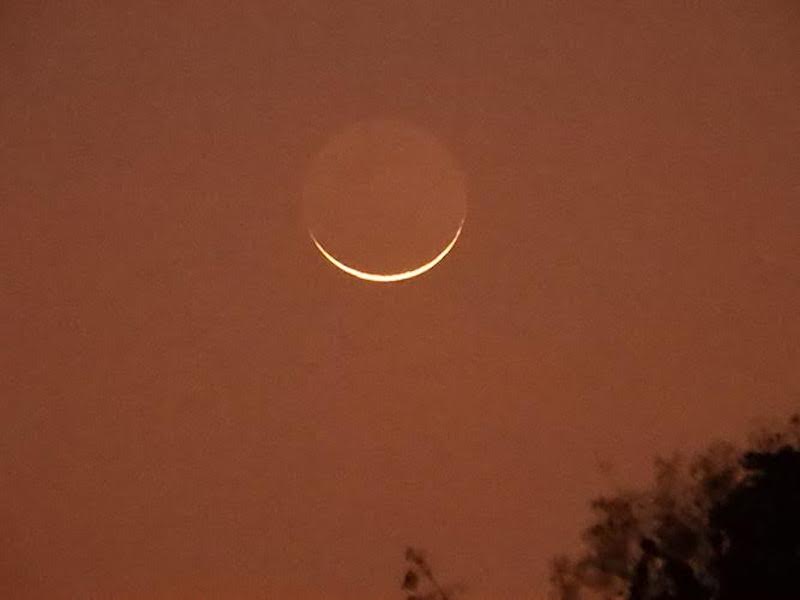 Very thin crescent moon with the rest of the moon faintly visible.