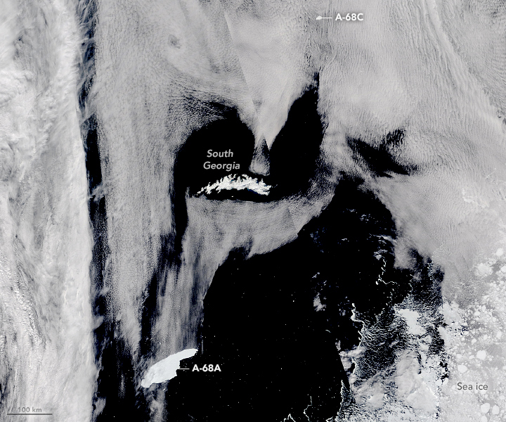 Orbital view of iceberg and island in white surrounded by gray clouds.