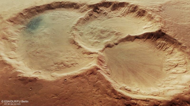 Aerial view of three overlapping craters with worn edges in a reddish landscape.