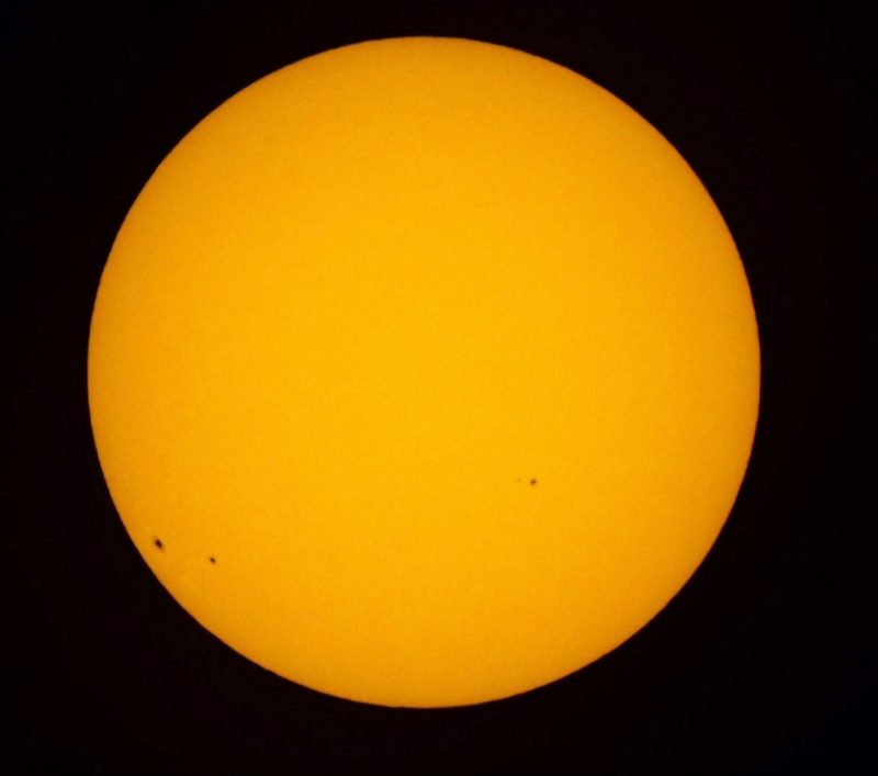 Telescopic image of the orange-yellow sun, showing several spots.
