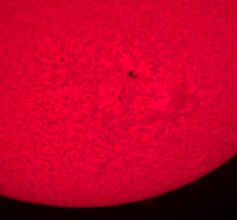 Section of sun's face in red with large sunspot having swirling magnetic fields radially around it.