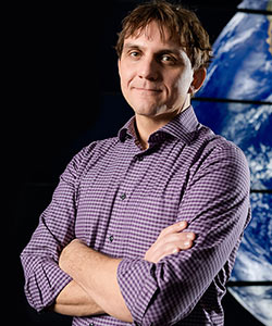 Man with his arms folded and a mural of Earth behind him.