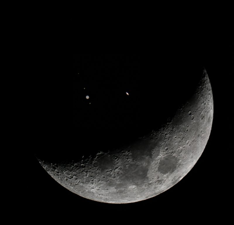 Crescent moon with two bright dots appearing on dark side.