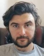 Intense-looking young man, with dark brown hair and clipped beard.