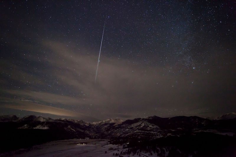 white streak on sky over dark mountains