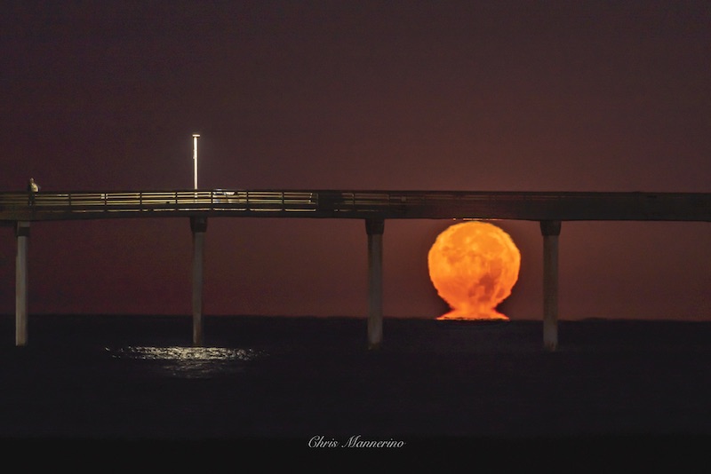 Moon rising over water under a bridge, sitting on a 'pedestal' of light.