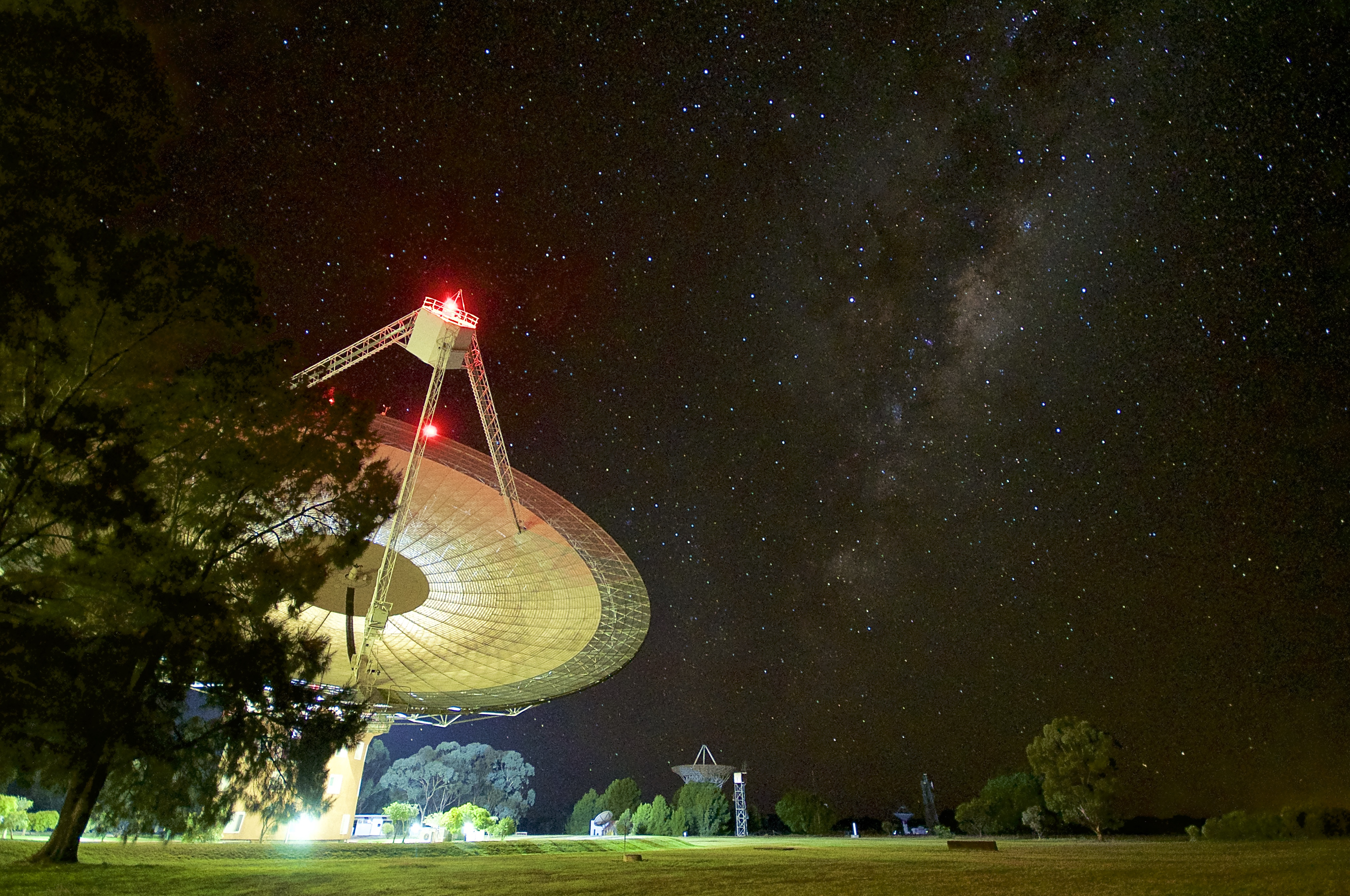 Radio telescope with lights on at night, and stars in the sky above.