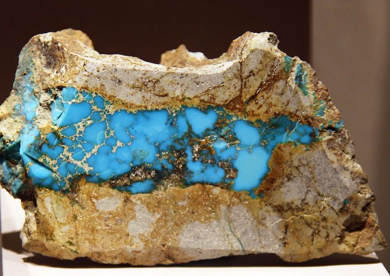 A rock of various shades of beige and brown, cut to reveal light blue turquoise in the middle that has beige veining.
