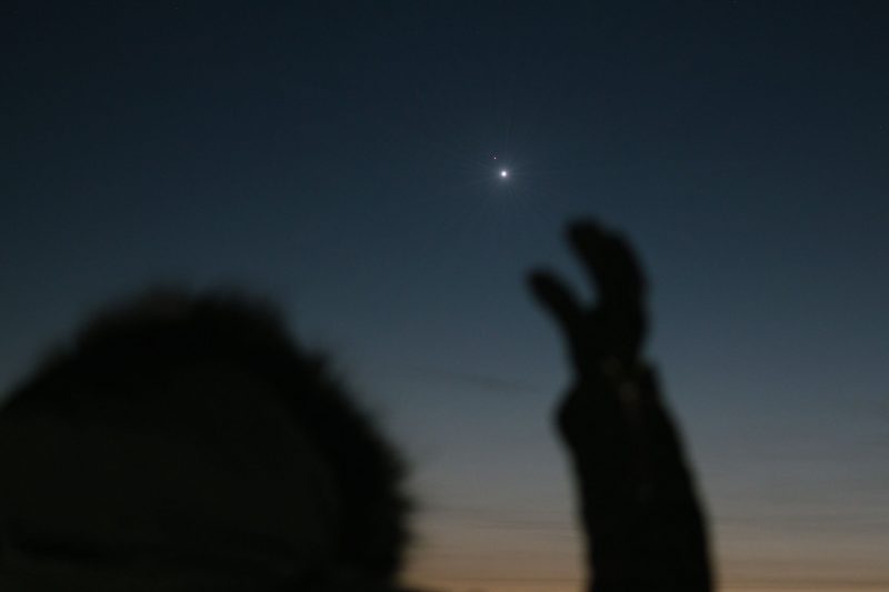 A man extending his arm to the sky, as if to hold the planets Jupiter and Saturn.