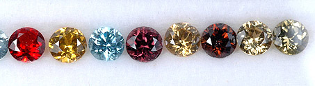 Eight small round cut zircon gemstones. One is clear, three are different shades of red, and four are different shades of yellow.