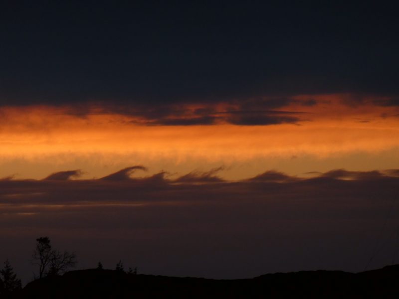 Dark sky with an orange strip through the middle and wave-like formations below.
