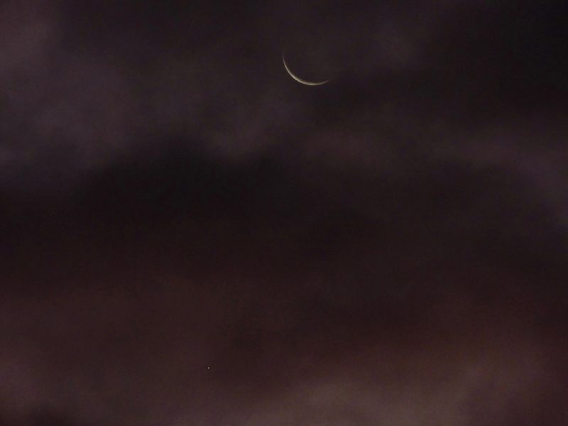 Large but very thin crescent moon over fuzzy clouds.