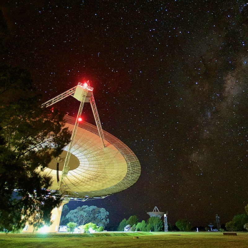 Dish-type radio telescope with lights on at night, and stars in the sky above.