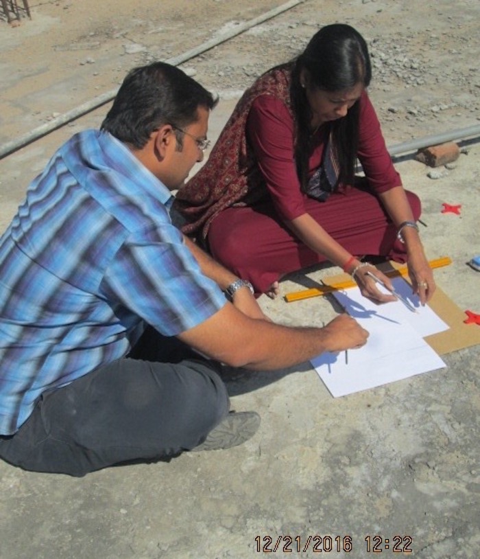 A man and a woman sitting on the ground measuring shadows on paper.