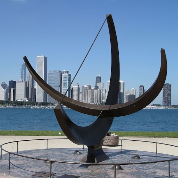Two large black metal semicircles at right angles with Chicago skyline in distance.