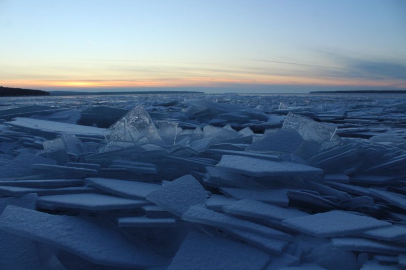 Slabs of ice at all angles piled up on each other under sunset sky.