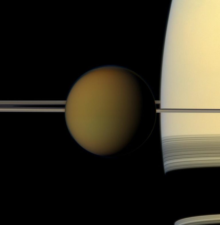 Hazy brownish ball with Saturn's thin rings on edge behind, and part of Saturn.