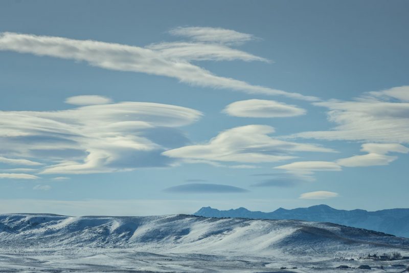 Snowy and mountainous landscape with white saucer-shaped lenticular clouds above.