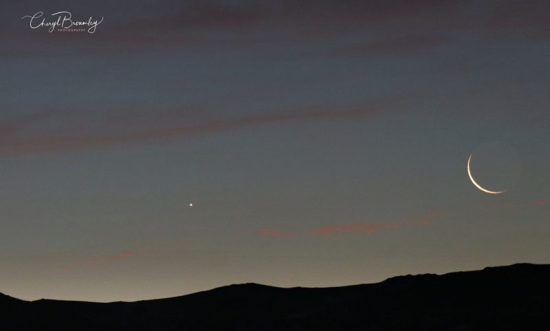 Venus and very thin crescent moon in slate blue sky near sunrise.