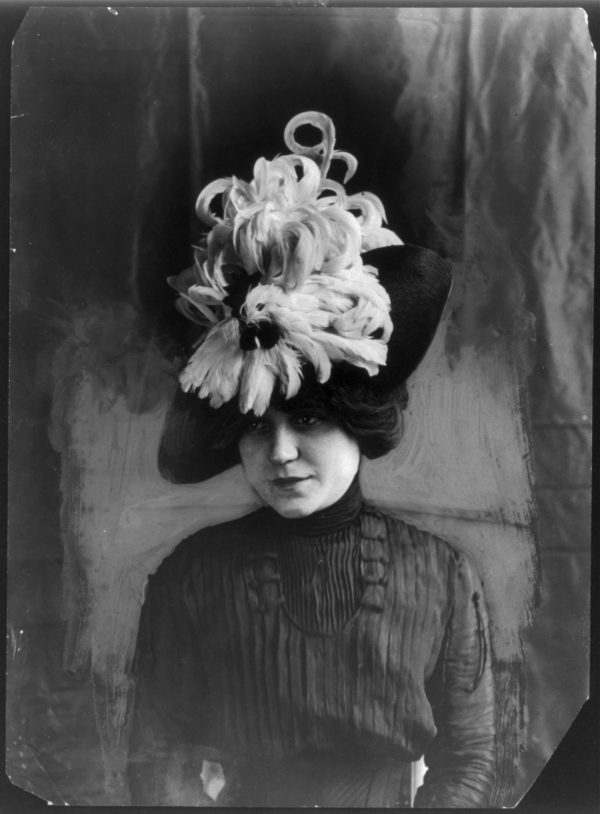 Woman in big hat with spray of dozens of feathers on it.