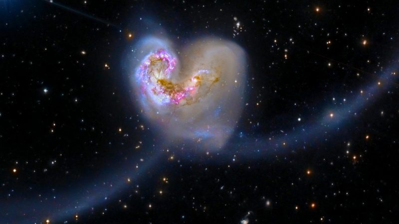 Two galaxies swirling together in a heart shape.