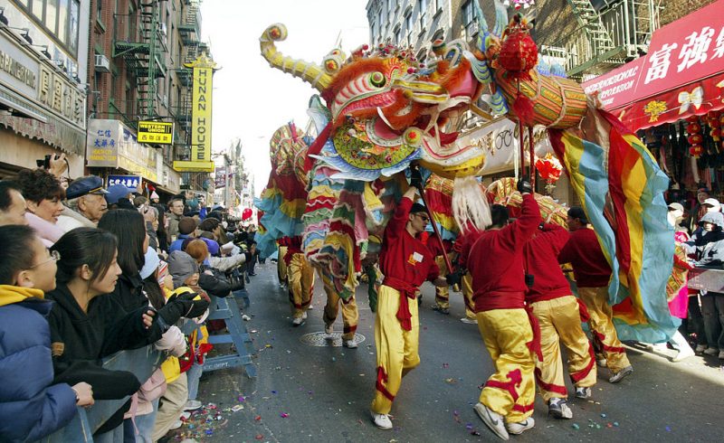 People in red and yellow carry a dragon float over their heads through a street lined with onlookers.