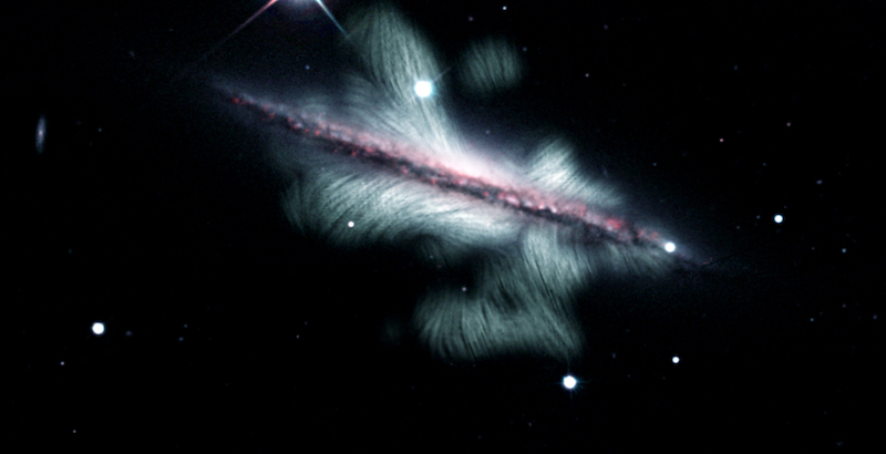 Side view of galaxy, with many white to minty-green wisps reaching away and out from it looking a bit like goldfish fins.