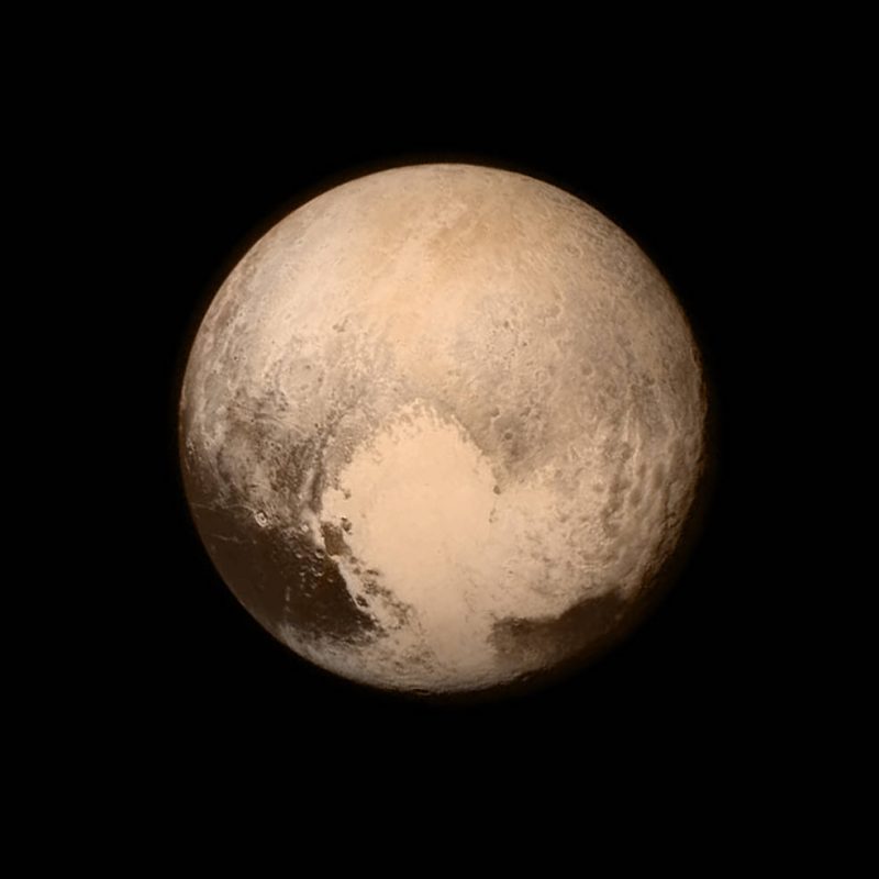 A beige and black surface of Pluto with the tracings of a large heart at bottom.