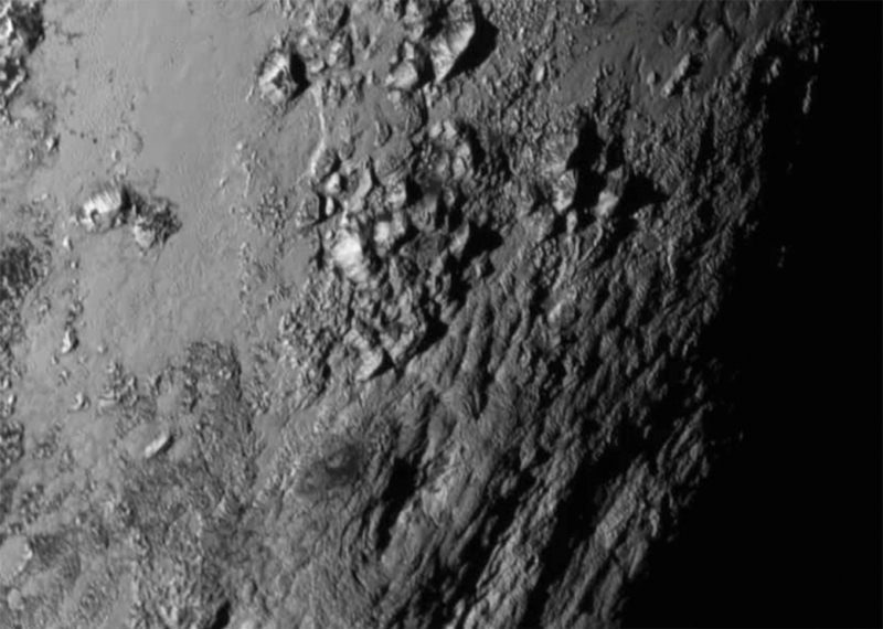 Pluto's rugged, irregular mountainous terrain in black and white from space.