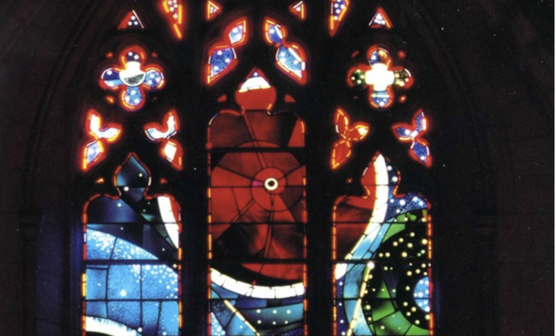 Large colored circles in a stained glass window, one with tiny black object in the middle.
