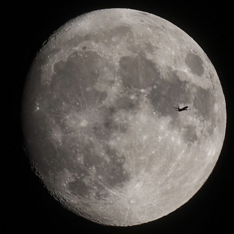 A nearly full moon with the small silhouette of an airplane crossing in front.