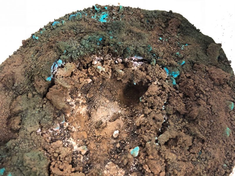 Crumbly, dark brown soil with very small blue and pink patches.