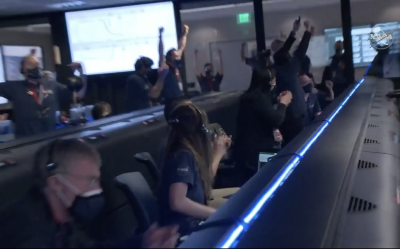 Flight engineers in a control room leaping up, waving their arms and cheering.