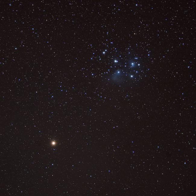 Red bright dot (Mars) at bottom left, blue star cluster (Pleiades) at top right, on black background.